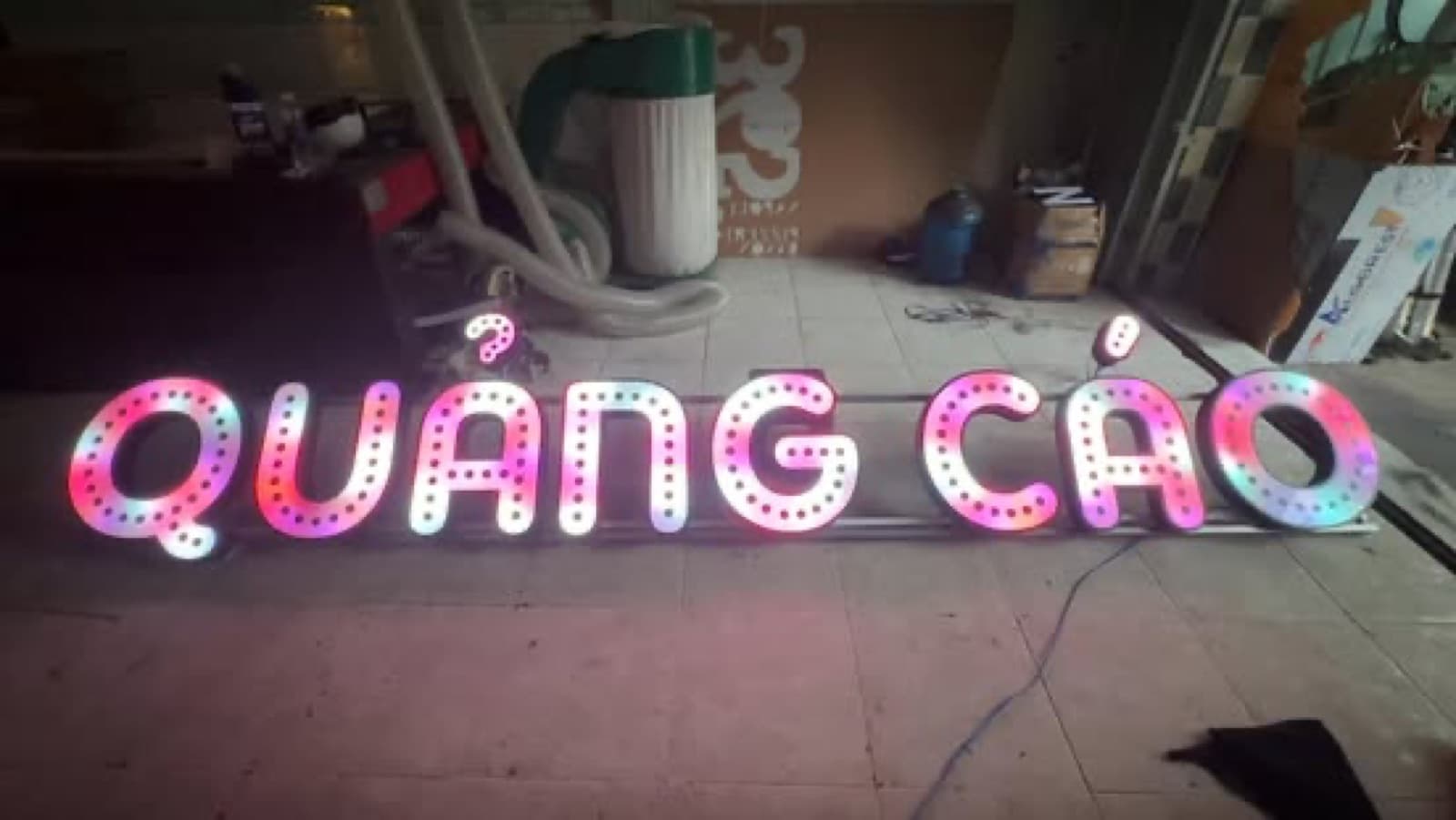 Bộ chữ Quang Cao nhiều màu đặt trên sàn, có dây điện và dụng cụ xung quanh