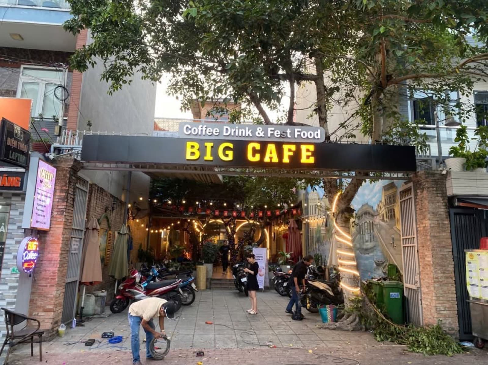 Bảng hiệu BIG CAFE phía trước cửa hàng, phía dưới có người và dụng cụ thi công